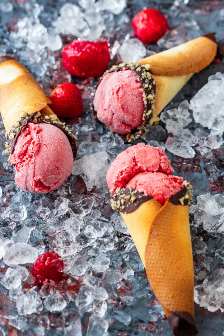 Three chocolate-dipped cones filled with strawberry ice cream and arranged on crushed ice.