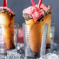 A scoop of strawberry ice cream in a chocolate-dipped, nut-rimmed cone set in a glass.