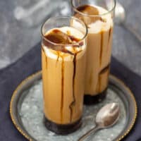 Two iced caramel lattes with foam, large ice cubes and caramel running down the glasses.
