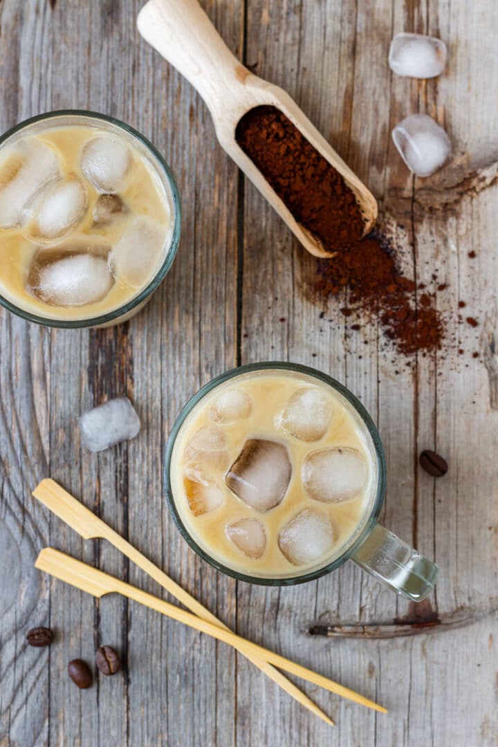 Overhead view of two glasses of iced coffee with ice cubes, instant coffee and scattered coffee beans.