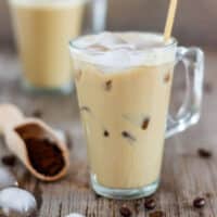 Close-up of lightly foamy instant iced coffee with ice cubes and a wooden stirrer.