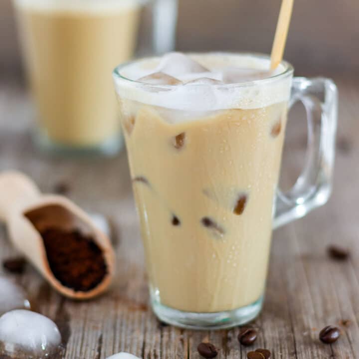 Close-up of lightly foamy instant iced coffee with ice cubes and a wooden stirrer.