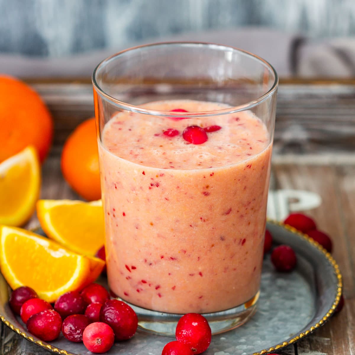 Cranberry orange smoothie in a glass with cranberries and sliced oranges.