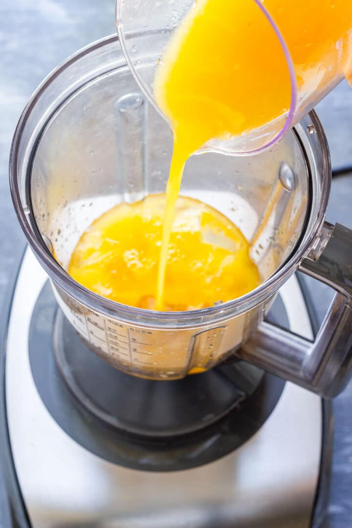 Freshly squeezed orange juice being poured into a blender with ice.