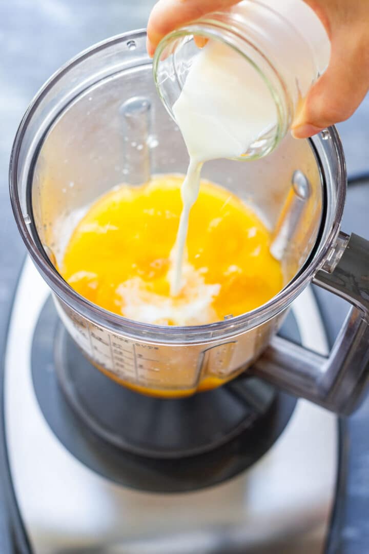 Milk being poured into the blender with orange juice and ice.