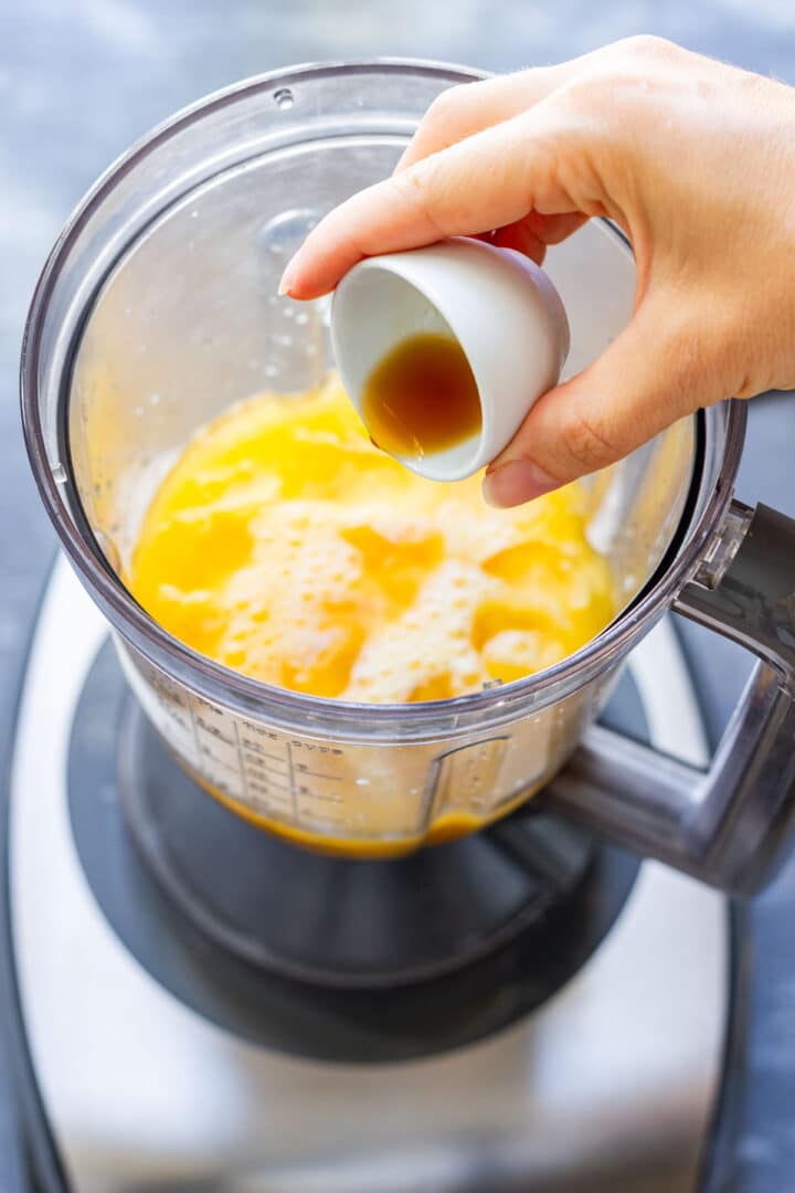 Vanilla extract being added to the orange juice mixture in the blender.