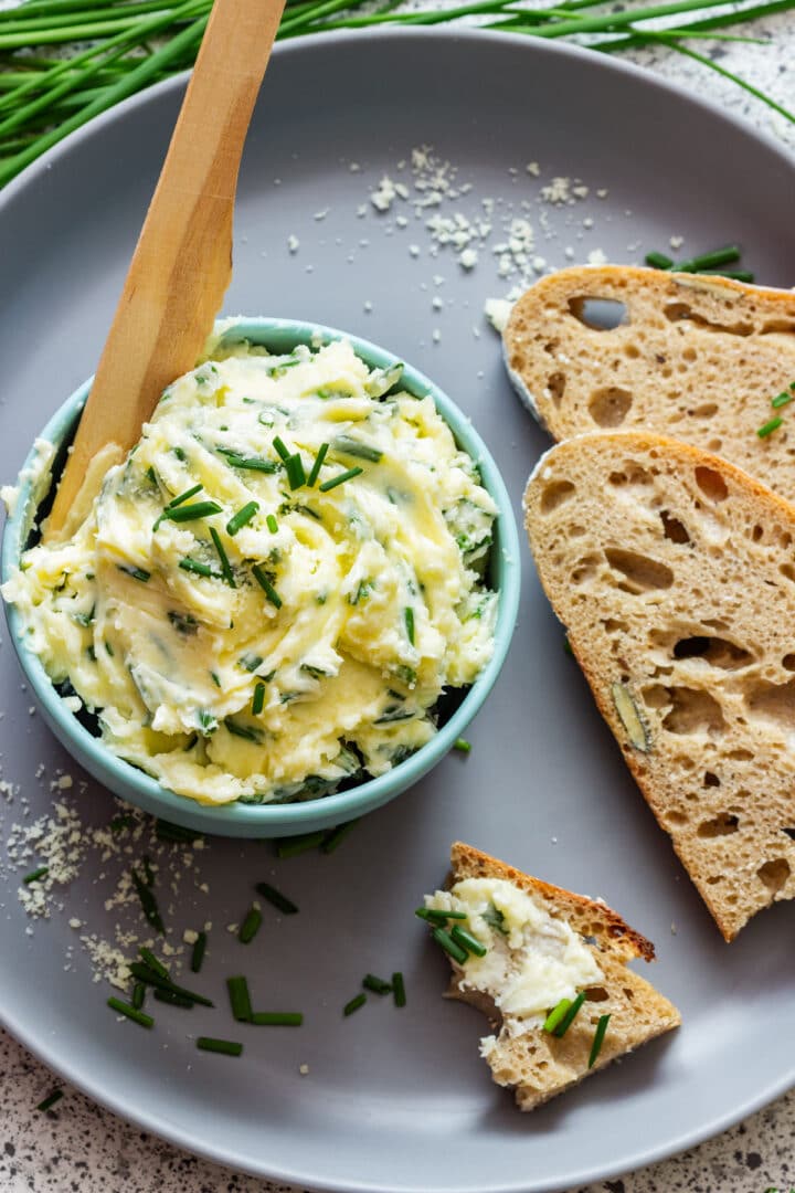 A piece of rustic bread spread with chive butter, with more butter in a bowl alongside.