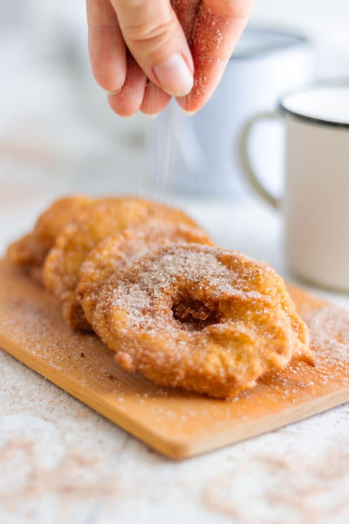Cinnamon sugar being sprinkled over freshly fried apple rings while they are still warm.