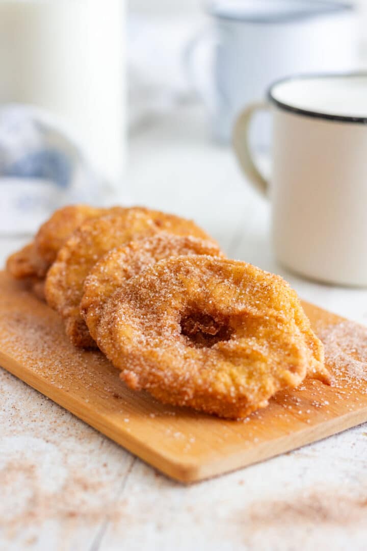 Three golden battered apple rings lined up after being coated in cinnamon sugar.