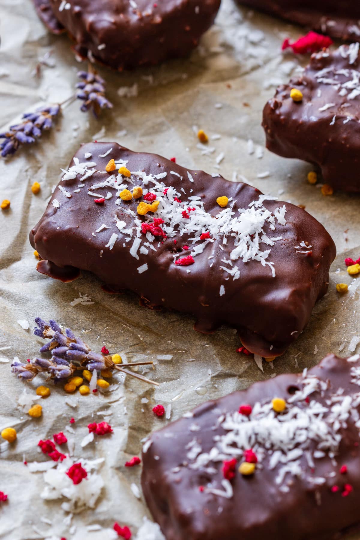 Homemade Bounty bar with a thick chocolate coating, shredded coconut, bee pollen and freeze-dried berries on top.