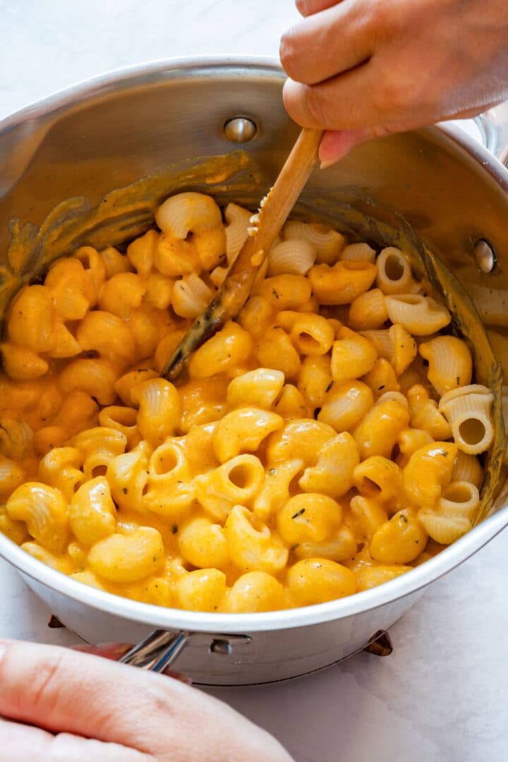 Cooked macaroni being stirred into the creamy sweet potato cheese sauce.