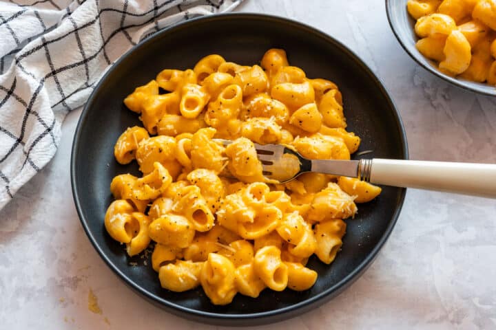 Sweet potato macaroni and cheese served on a black plate with black pepper and grated cheddar.
