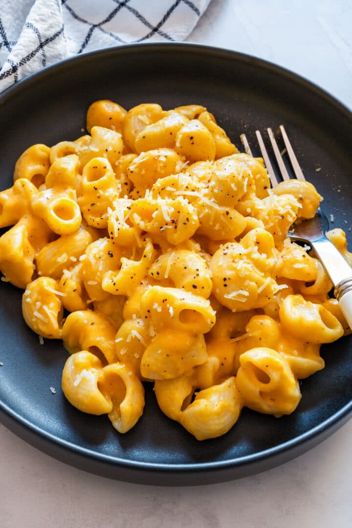 Close-up of macaroni coated in creamy orange sweet potato sauce with black pepper and grated cheddar.