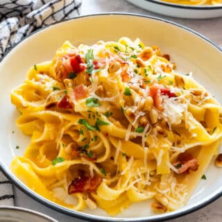 A plate of butternut squash pasta with crispy bacon, toasted pine nuts, Parmesan and fresh parsley.