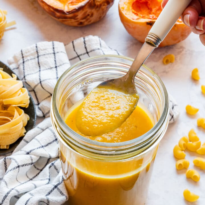 Spoonful of smooth, thick roasted butternut squash sauce held over a full jar.