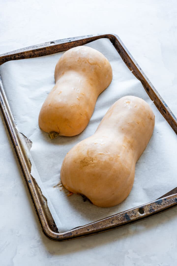 Butternut squash halves placed cut-side down on a parchment-lined baking sheet.