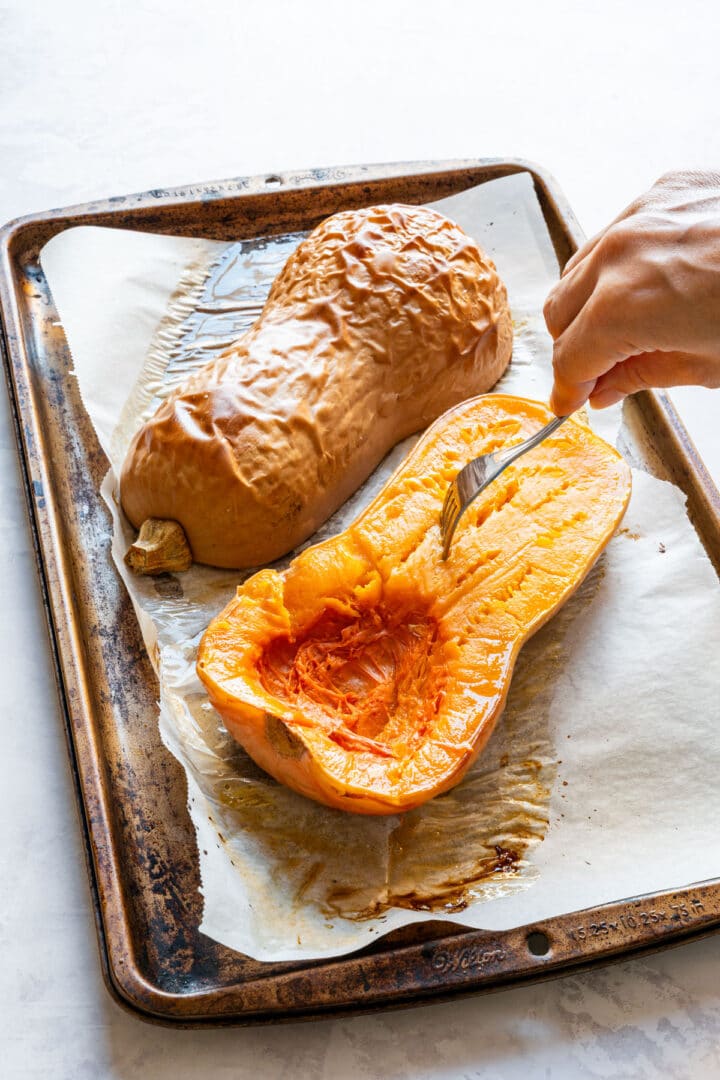 A fork checking the roasted butternut squash flesh to make sure it is soft.