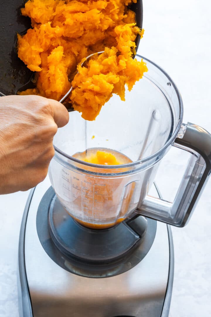 Roasted butternut squash flesh being transferred to a blender.