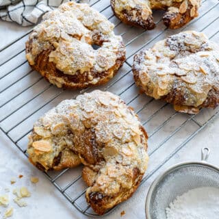 Almond croissants with golden almond topping and powdered sugar on a wire cooling rack.