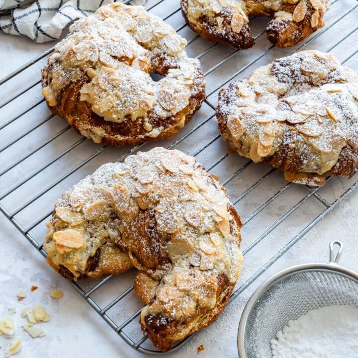 Almond croissants with golden almond topping and powdered sugar on a wire cooling rack.