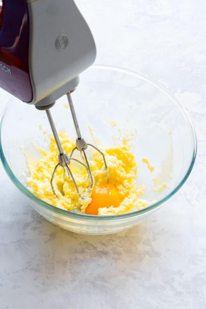 Egg being mixed into creamed butter and sugar with an electric hand mixer.