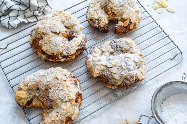 Baked croissants with golden sliced almonds and a dusting of powdered sugar, cooling on a wire rack.