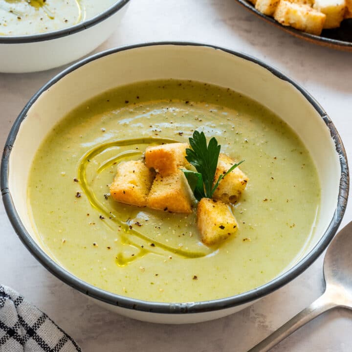 Close-up of broccoli and cauliflower soup topped with golden croutons, a parsley leaf, black pepper and olive oil.